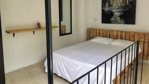 Une chambre à coucher avec une tête de lit en bois, un couvre-lit blanc, une étagère en bois et un tableau accroché au mur.