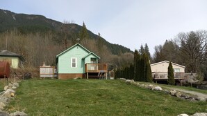 A light green house with a deck, surrounded by a stone wall and a grassy yard.