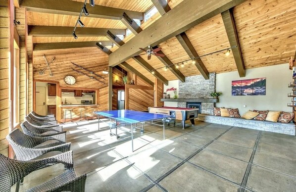 A spacious indoor area with a ping pong table, wicker chairs, a fireplace, and a stone wall.