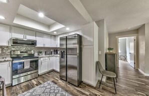 A modern kitchen with stainless steel appliances, white cabinetry, and a patterned rug.