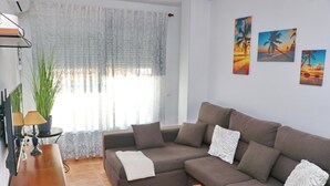A living room with a brown sofa, a wooden side table, and a lamp. There are three paintings on the wall.