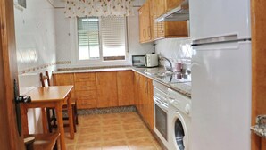 A compact kitchen with wooden cabinets, a built-in microwave, a washing machine, and a dining table with chairs.