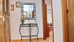 A hallway with a wooden door, a mirror, a small table with a vase of flowers, and a tiled floor.