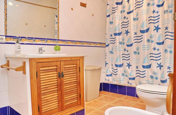 A bathroom with a wooden cabinet, a sink, a toilet, and a shower curtain with a nautical theme.