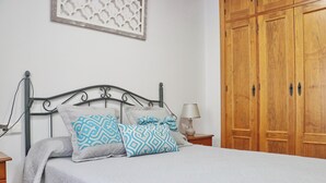 A bedroom with a bed, a nightstand, a lamp, and wooden wardrobes.