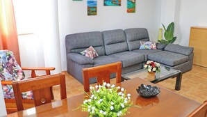 A living room with a grey sofa, wooden chairs, a glass coffee table with a flower arrangement, and paintings on the wall.