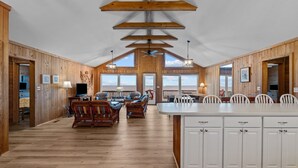 A spacious room with wooden walls and a large island with white cabinets. There are two large windows providing natural light and a view of the outdoors. - 2877 - Carolina Dreamin - Oceanfront Duck Escape w/ Hot Tub & Views (Kitty Hawk)