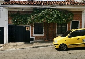 Um táxi amarelo estacionado em frente a um prédio com portão preto e placa de 'Proibido Estacionar'.