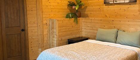 Habitación con paneles de madera, una cama, un ventilador de techo, una puerta y una planta en la pared.