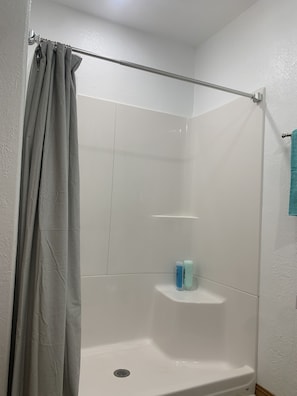 Une douche avec un rideau à rayures, un mur recouvert de carreaux blancs et une serviette bleue accrochée au mur.