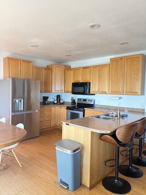 A modern kitchen with wooden cabinets, stainless steel appliances, a granite countertop, and a bar stool area. - Cozy beach front lake cabin with hot tub! (Lake Norden)