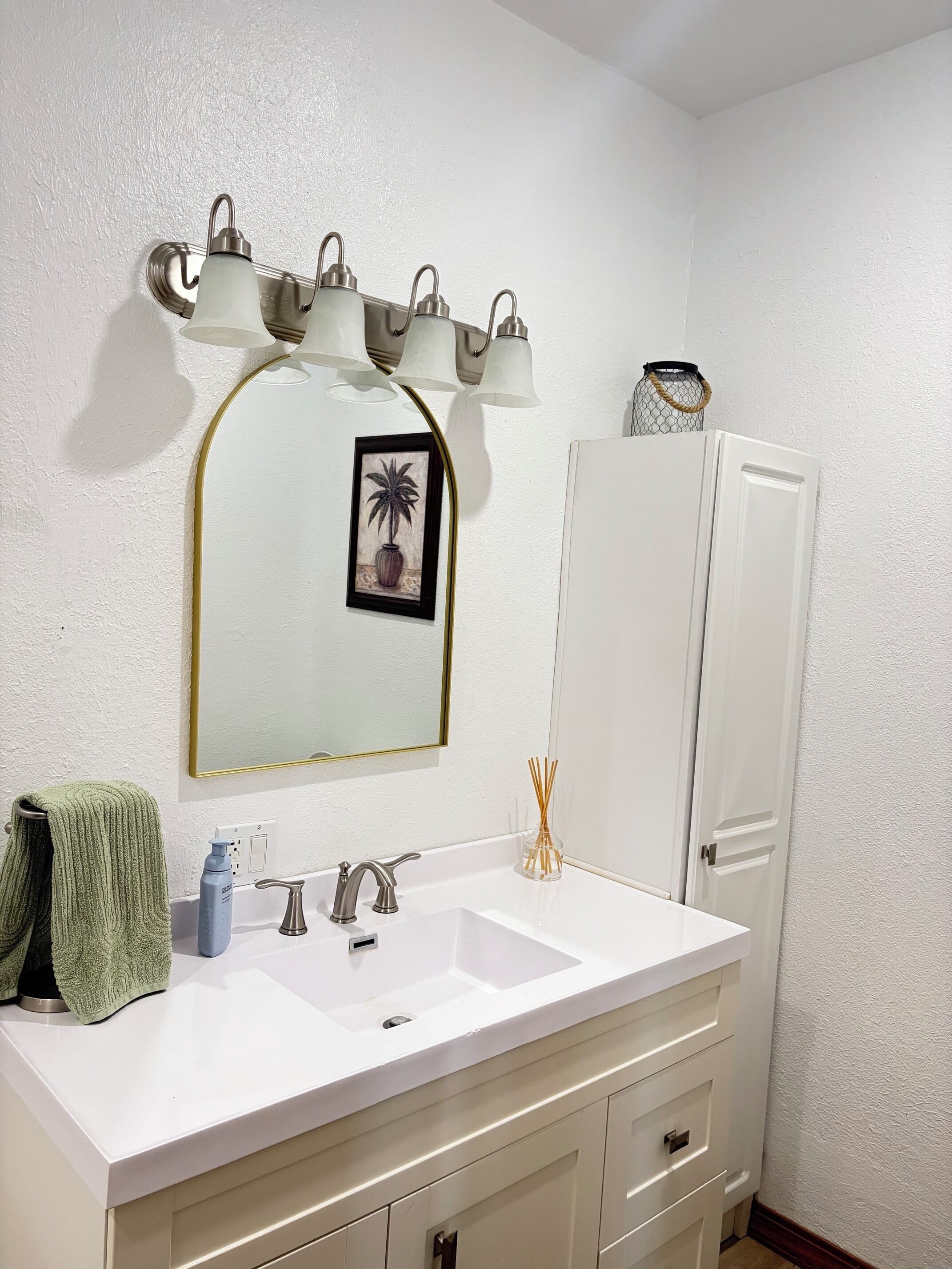 Une salle de bain avec un lavabo blanc, un miroir avec un cadre doré et un porte-serviettes.