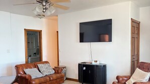 Ein Wohnzimmer mit Deckenventilator, Flachbildfernseher an der Wand und Ledersofas.