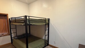 Ein Stockbett in einem Zimmer mit Holzboden, einem Fenster mit Jalousien und einem kleinen Tisch.