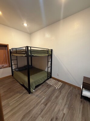 A bunk bed in a room with wooden flooring, a window with blinds, and a small table. - Cozy beach front lake cabin with hot tub! (Lake Norden)