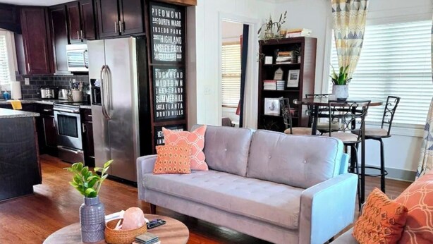 Een moderne woonkamer met een grijze bank, een ronde salontafel en een eethoek met een houten tafel en stoelen.