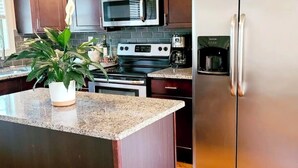 Een keuken met donkere houten kasten, roestvrijstalen apparatuur waaronder een magnetron, oven en koelkast, een granieten aanrechtblad en een potplant.
