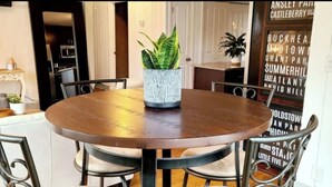 Een ronde houten eettafel met vier stoelen, een potplant en een decoratieve muur met tekst.