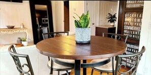 A round wooden dining table with four chairs, a potted plant, and a decorative wall with text.