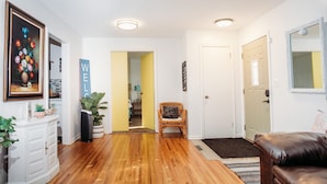 A well-lit hallway with wooden flooring, a wicker chair, a brown leather sofa, and a door leading to another room. - Welcome to our charming and newly remodeled home, close to everything (Richfield)