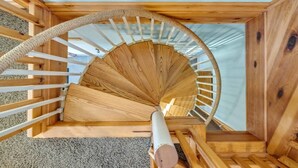 Un escalier en colimaçon en bois, doté d’une rampe en corde, de marches recouvertes de moquette et d’une lucarne au-dessus.