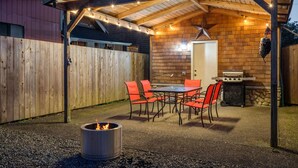 Une terrasse extérieure avec un foyer, un barbecue et une table avec des chaises.