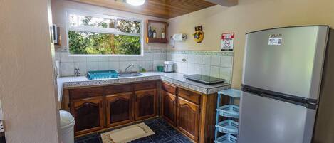 A kitchen with wooden cabinets, a refrigerator, and a window with a view of greenery.