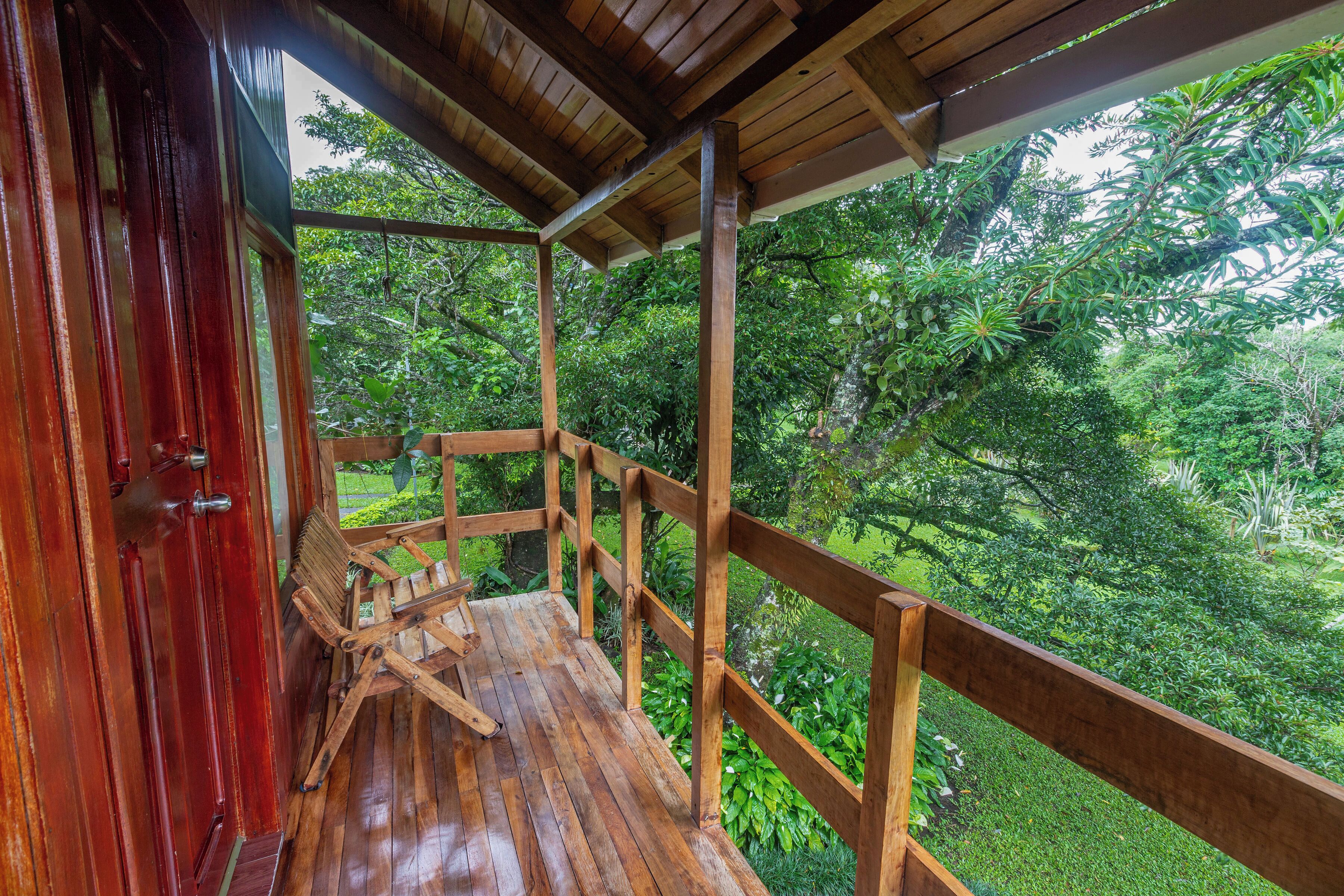 Un terrazza in legno con una panchina e una porta, con vista su un rigoglioso giardino.