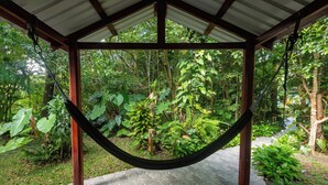 A hammock under a wooden pergola in a lush garden with stone flooring.