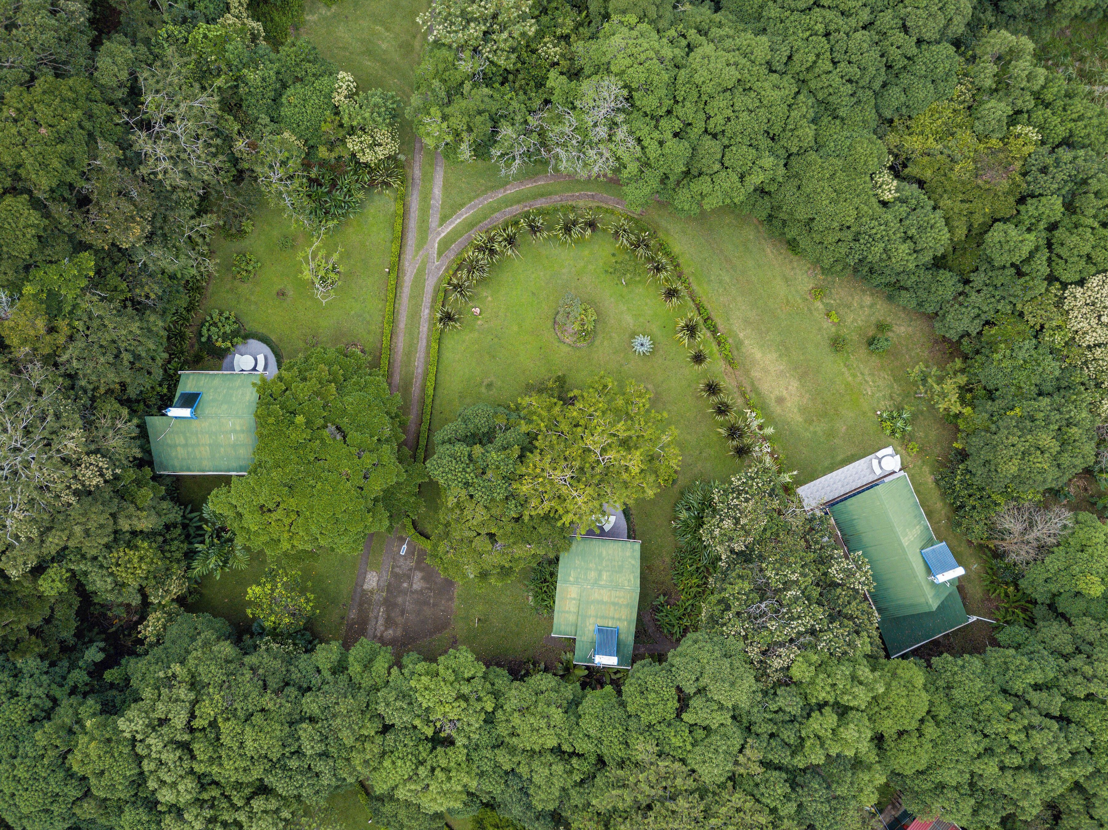 An aerial view of a property with three green-roofed buildings surrounded by dense forest.