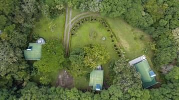 An aerial view of a property with three green-roofed buildings surrounded by dense forest.