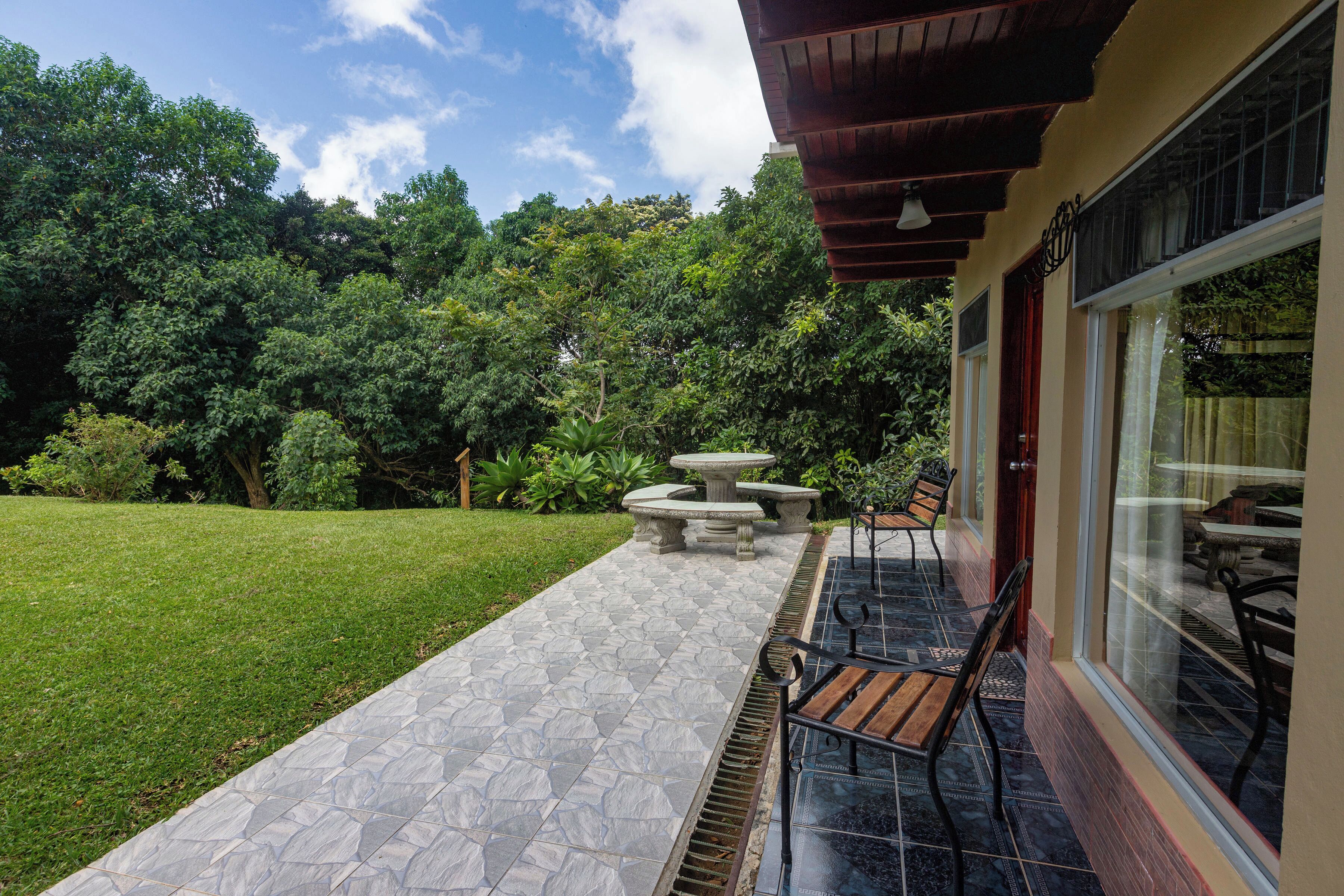 A patio with stone flooring, outdoor furniture, and a view of a lush garden and trees.