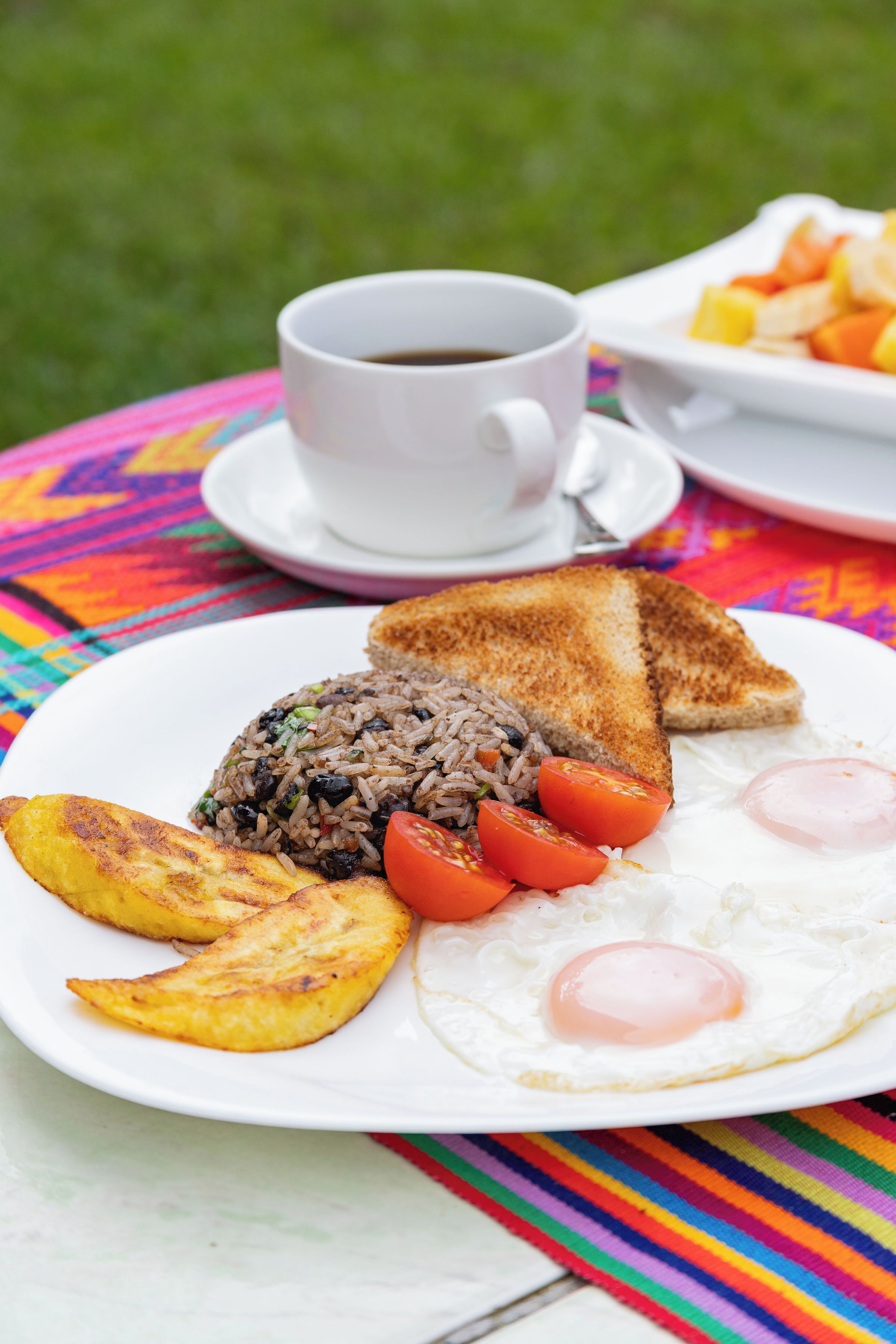 A plate of breakfast food including toast, fried rice, eggs, and plantains on a colorful tablecloth.