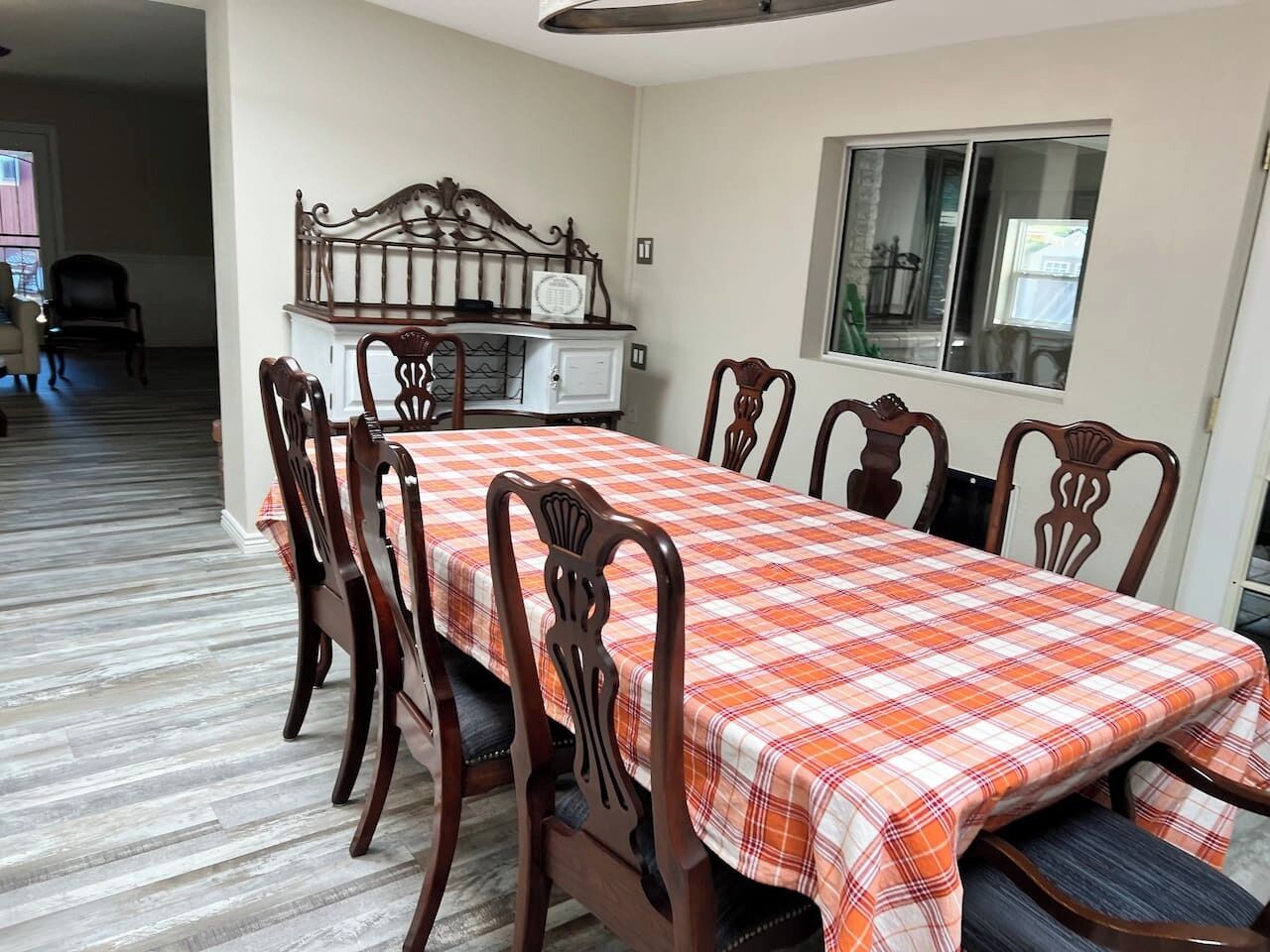 A dining room with a checkered tablecloth, wooden chairs, a microwave, and a window.