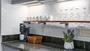Une cuisine avec des carreaux de céramique blancs disposés en motif métro, une machine à café, un panier et une plante en pot.
