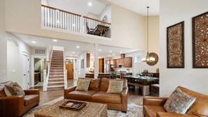 A spacious living area with a high ceiling, a staircase leading to an upper level, and a kitchen in the background. - Luxurious Retreat in SW Portland with 7-Person Hot Tub – Sleeps 14 Comfortably! (Portland)