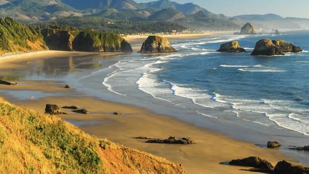 A coastal landscape with a sandy beach, rocky outcrops, and distant mountains. - Luxurious Retreat in SW Portland with 7-Person Hot Tub – Sleeps 14 Comfortably! (Portland)