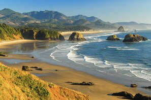 A coastal landscape with a sandy beach, rocky outcrops, and distant mountains. - Luxurious Retreat in SW Portland with 7-Person Hot Tub – Sleeps 14 Comfortably! (Portland)