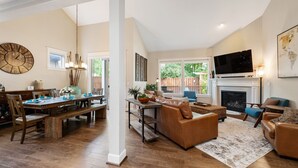 A spacious living room with a fireplace, a dining area with a wooden table and chairs, and a large clock on the wall. - Luxurious Retreat in SW Portland with 7-Person Hot Tub – Sleeps 14 Comfortably! (Portland)