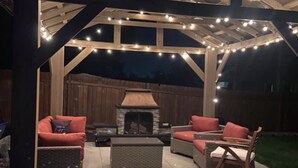 An outdoor patio with a covered seating area, a stone fireplace, and string lights. - Luxurious Retreat in SW Portland with 7-Person Hot Tub – Sleeps 14 Comfortably! (Portland)