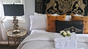 Ein ordentlich bezogenes Bett mit weißen und orangefarbenen Kissen, ein dekorativer Kopfteil und ein Nachttischchen mit Lampe.