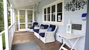 Eine überdachte Veranda mit Korbmöbeln, einem Willkommensschild und einer Tafel zur Buchung.