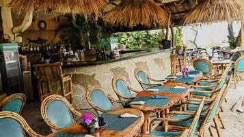 Un restaurante con mobiliario de bambú, una zona de bar y un techo de paja.