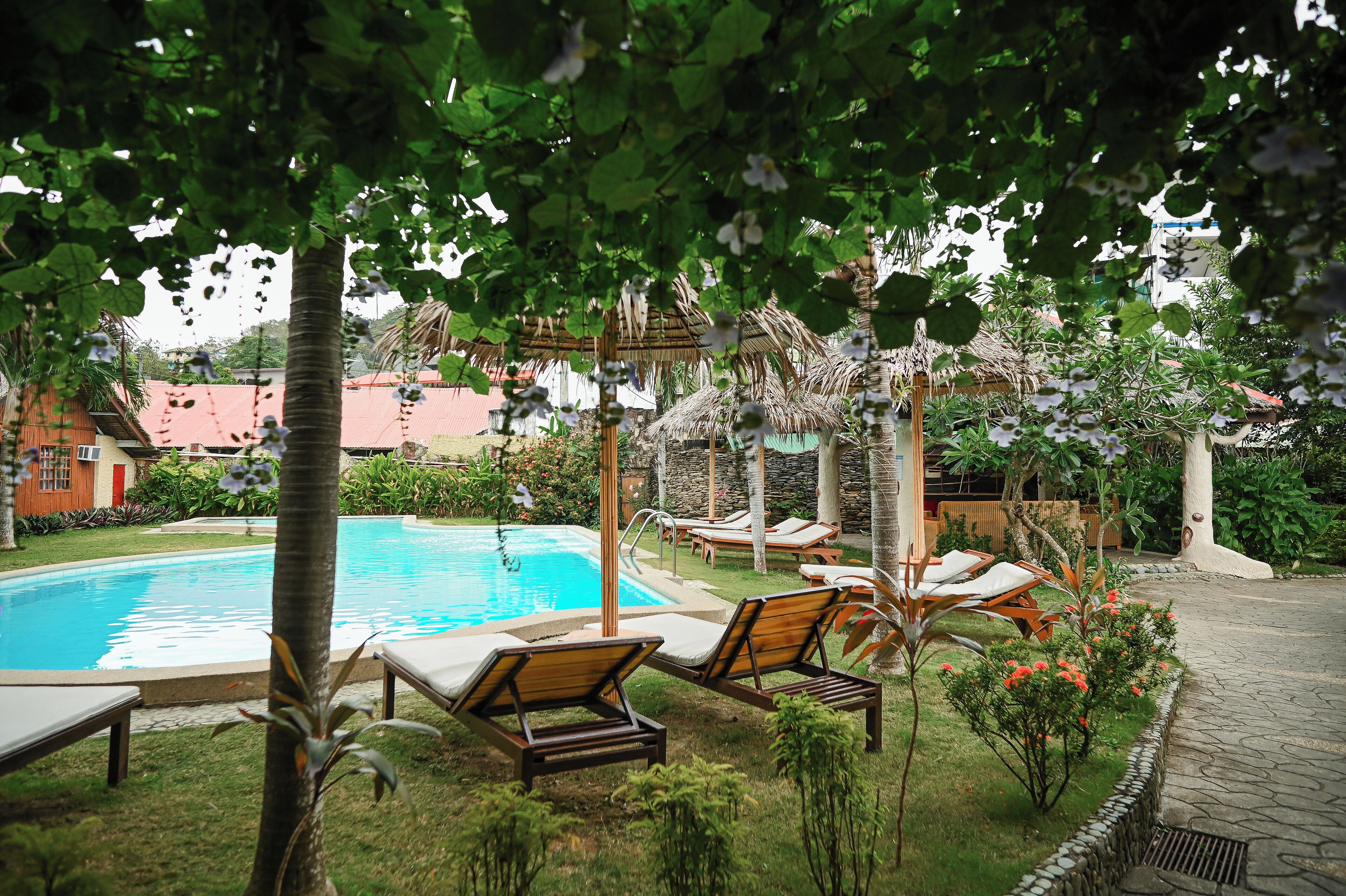 Piscina con sillas de descanso, rodeada de follaje y un sendero de piedra.