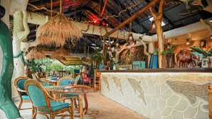 Un restaurante con un interior rústico, que presenta muebles de madera, una barra de piedra y decoración tropical.