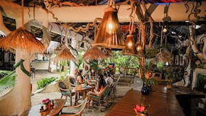 Un comedor interior con mesas y sillas de madera, lámparas colgantes y decoración tropical.