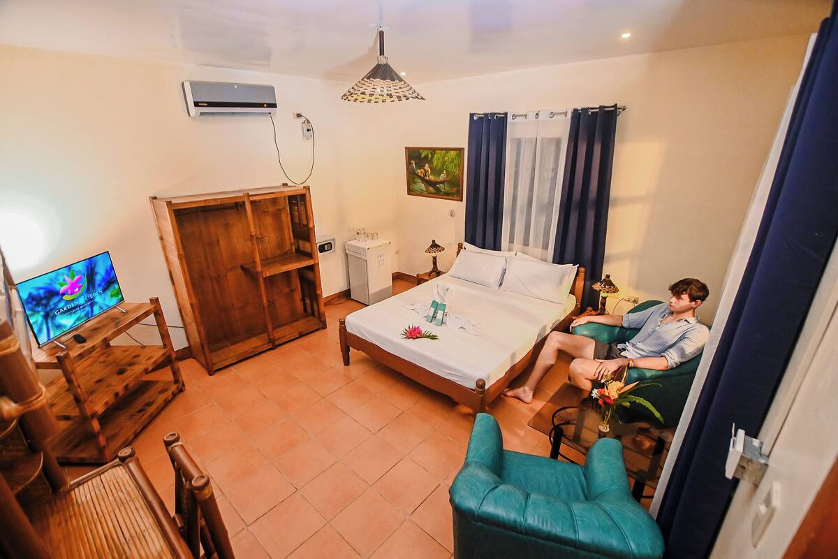 A bedroom with a bed, a TV, a wooden wardrobe, a desk, and a chair.