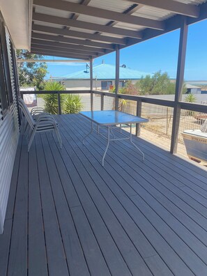 Eine überdachte Terrasse mit Tisch und Stühlen, Blick auf ein Haus mit blauem Dach und einem umzäunten Garten.