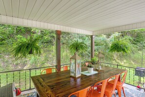 Un espace extérieur abrité, aménagé pour les repas, avec une table en bois et des chaises orange, le tout entouré de verdure.
