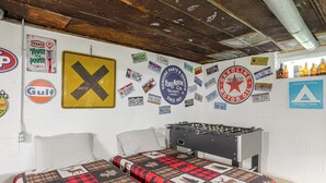 A room with two beds, a foosball table, and a wall decorated with various license plates and signs. - Fire Pit & Game Room: Family Home in Marshall! (Marshall)